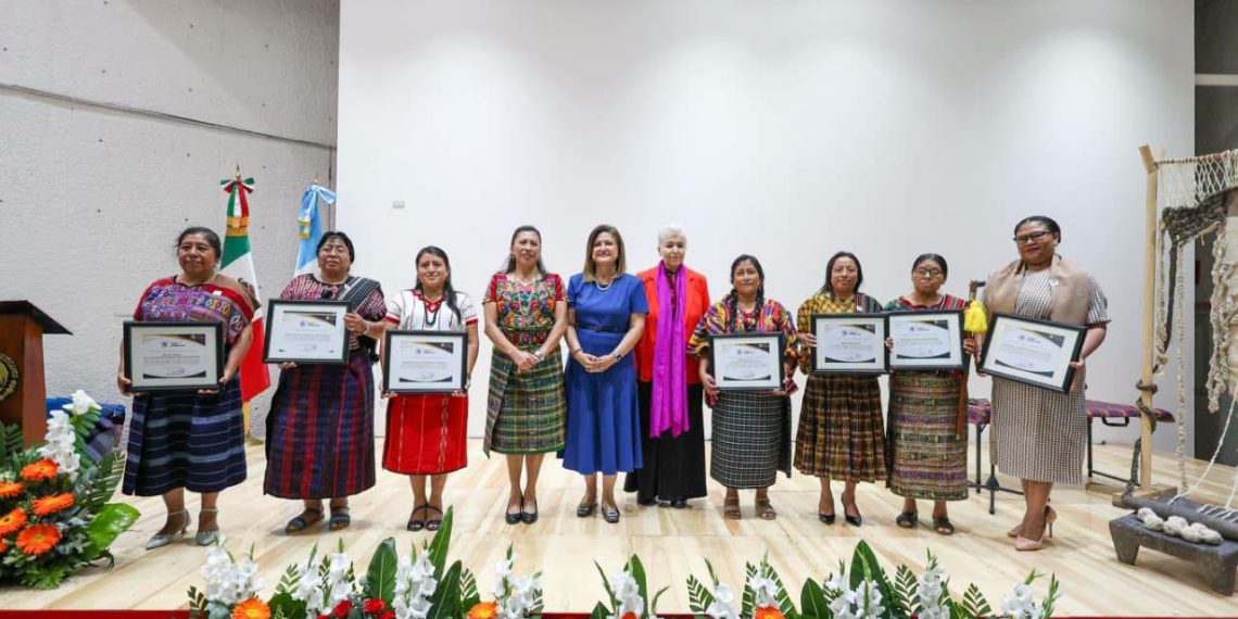 Siete mujeres indígenas distinguidas con la Orden Ütz Samaj sosteniendo sus diplomas y condecoraciones durante la ceremonia oficial.
